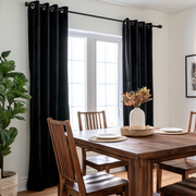 Cozy dining room with black grommet curtains, warm wooden furniture, and fresh greenery