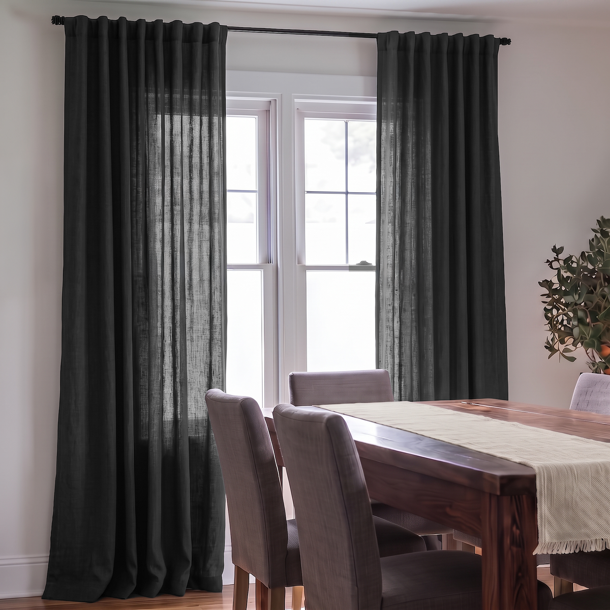 Floor-length charcoal gray curtains filter light through a dining room window beside a dark wooden table with a beige runner and gray upholstered chairs