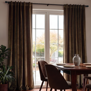 Inviting dining room with chocolate brown back-tab curtains, dark wooden furniture, and warm sunlight.