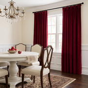 An elegant traditional dining room with deep burgundy curtains, a round white pedestal table, upholstered classic chairs, a crystal chandelier, and a decorative bowl of pomegranates