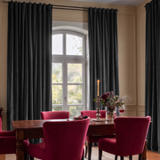 A dramatic dining room with charcoal-black curtains, a dark wooden table, rich burgundy velvet chairs, candlelight, red wine, and a moody floral arrangement