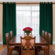 Classic dining room with emerald green grommet curtains, carved wooden furniture, and elegant red roses.