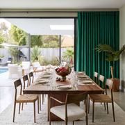 Modern dining room with emerald green S-fold curtains, wooden furniture, and an inviting poolside view
