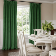 Elegant dining room with deep green pinch-pleat curtains, white furniture, and fresh botanical décor.