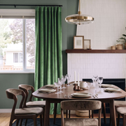 Modern dining room with deep green S-fold curtains, sculptural wooden chairs, and elegant lighting.
