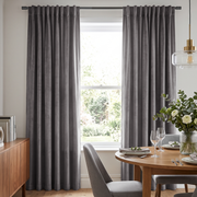 A bright contemporary dining room with elegant gray curtains, a round wooden table, gray upholstered chairs, refined place settings, fresh flowers, and a modern glass pendant light