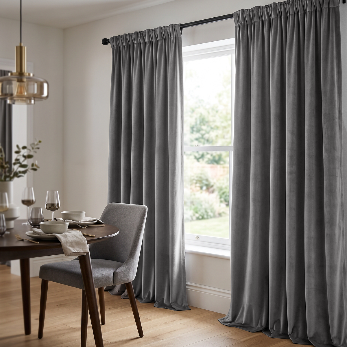 A modern dining room with floor-length gray curtains, a dark wooden table, upholstered gray chairs, elegant tableware, and warm contemporary pendant lighting
