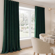 A bright elegant dining space with luxurious forest-green curtains, a large garden-facing window, cream upholstered chairs, a softly dressed table, and modern glass lighting