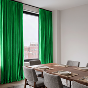 Modern dining room with vivid green S-fold curtains, contemporary furniture, and a city view.
