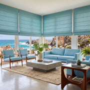 Aquamarine Roman Blinds in a Coastal Sunroom with White Walls, Light Blue Armchairs and a Coffee Table.