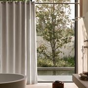 Natural Linen Hookless Shower Curtain in a Modern Bathroom with Beige Stone Walls and Freestanding Tub