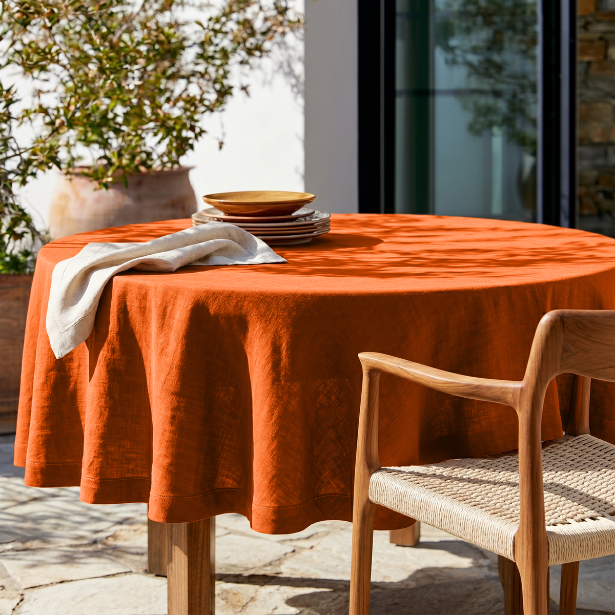 Burnt Orange Linen Round Tablecloth in a Sunlit Patio Dining Space with Stone Flooring and Natural Wood