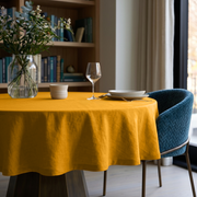 Mustard Yellow Linen Round Tablecloth in a Cozy Dining Nook with Warm Wood Shelving and Deep Blue Velvet Chairs