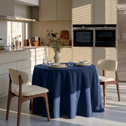 Royal Blue Linen Round Tablecloth in a Modern Kitchen Dining Space with Cream Cabinetry and Bouclé Chairs