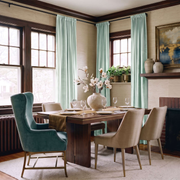 Elegant dining room with pale sage rod-pocket curtains, rich wood accents, and modern upholstered chairs.

