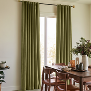 Warm dining room with olive green back-tab curtains, wooden furniture, and soft natural light.
