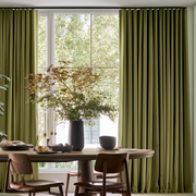 Modern dining room with olive green S-fold curtains, wooden furniture, and lush natural greenery.