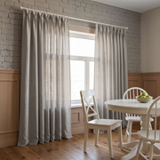 Natural Linen Pinch Pleat Curtains in a Dining Room with Grey Brick Walls, a White Table and Matching Wooden Chairs.
