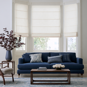 Off-White Roman Blinds in a Living Room with White Walls and a Blue Sofa and Wooden Coffee Table
