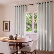 Bright dining room with white grommet curtains, warm wooden furniture, and a peaceful garden view.
