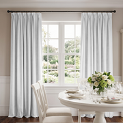 Elegant dining room with white pinch-pleat curtains, classic furniture, and a beautiful garden view.
