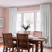 Charming dining room with white rod-pocket curtains, woven chairs, and soft blush-pink walls.
