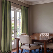 Refined dining room with olive green back-tab curtains, dark wooden furniture, and classic upholstered chairs