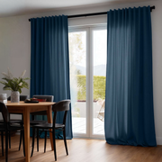 Floor-length teal blue curtains frame glass patio doors beside a wooden dining table with black chairs and a vase of greenery and white flowers