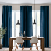 Floor-length teal blue curtains hang across tall dining room windows behind a wooden table with white chairs and two black pendant lights