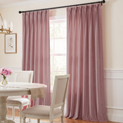 A soft, elegant dining room with dusty-pink curtains, a round white table, cream upholstered chairs, delicate floral décor, and warm natural light