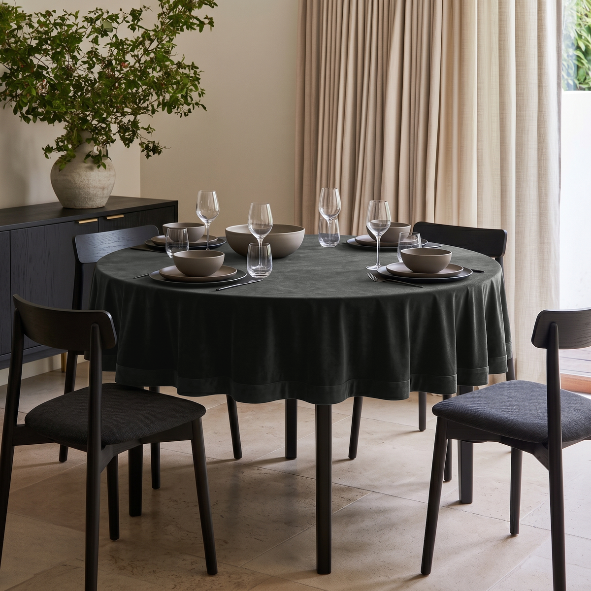 Dark Grey Round Velvet Tablecloth in a Contemporary Dining Room with Beige Curtains and Black Wood Accents