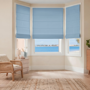 Sky Blue Cordless Linen Roman Blinds in a Coastal Bedroom with Cream Walls and a Rattan Armchair