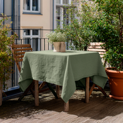 Asparagus Green Square Linen Tablecloth on a Sunny Urban Balcony with Wooden Furniture