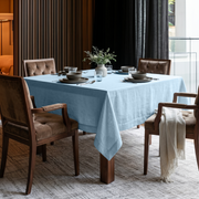 Sky Blue Square Linen Tablecloth in a Contemporary Dining Room with Brown Upholstered Chairs and Dark Floor-to-Ceiling Curtains
