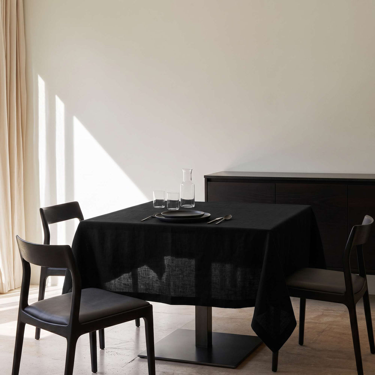 Black Square Linen Tablecloth in a Minimal Dining Room with Cream Walls and Dark Wood Chairs