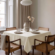 Cream Square Linen Tablecloth in a Bright Transitional Dining Room with Cane Chairs and Neutral Curtains