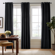 A bright modern dining room with tall windows, elegant black curtains, a dark wooden table, a beige upholstered chair, fresh flowers, and a large indoor plant