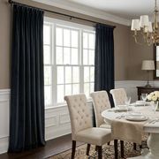 A classic dining room with floor-length black curtains, a round white table, tufted cream chairs, elegant place settings, and traditional brass lighting
