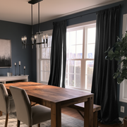 A stylish dining room with charcoal walls, floor-length black curtains, a large rustic wooden table, upholstered chairs, modern pendant lighting, and a leafy indoor plant