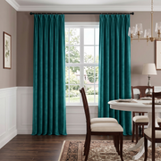 A classic dining room with rich teal curtains, a round white table, wooden chairs with cream upholstery, traditional wall paneling, and elegant brass lighting