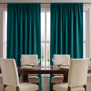 An elegant dining room with rich teal curtains, a dark wooden table, cream upholstered chairs, crystal glassware, white tableware, and slender gold candlesticks